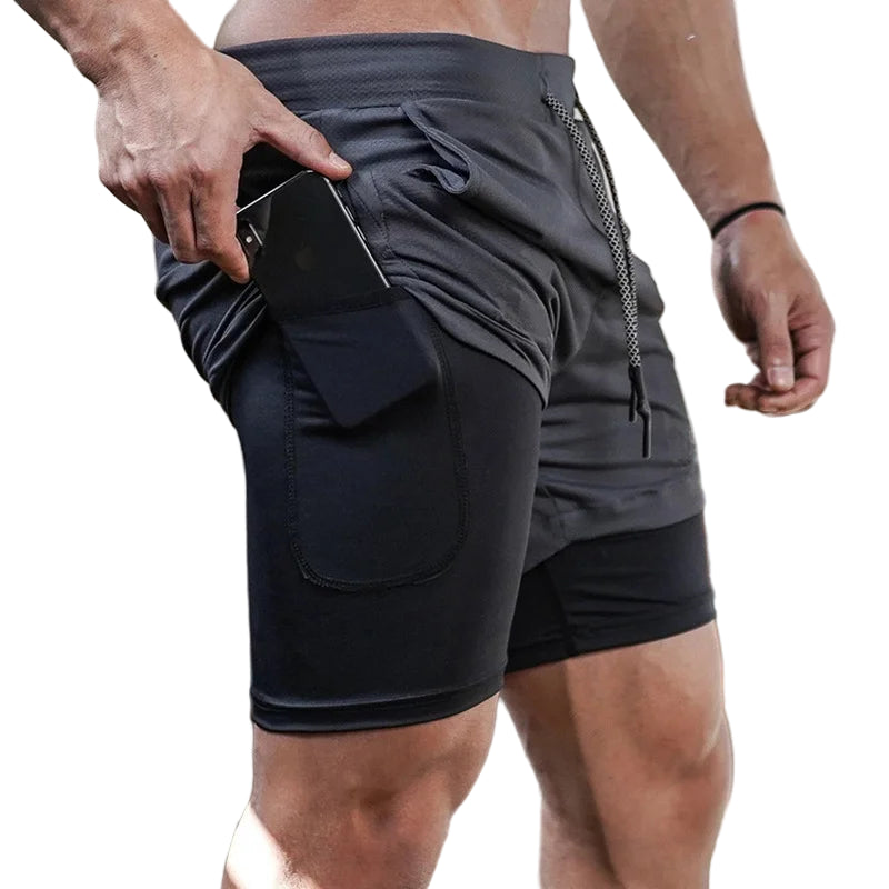 Person wearing black athletic shorts with a pocket, holding a phone, in an indoor setting.